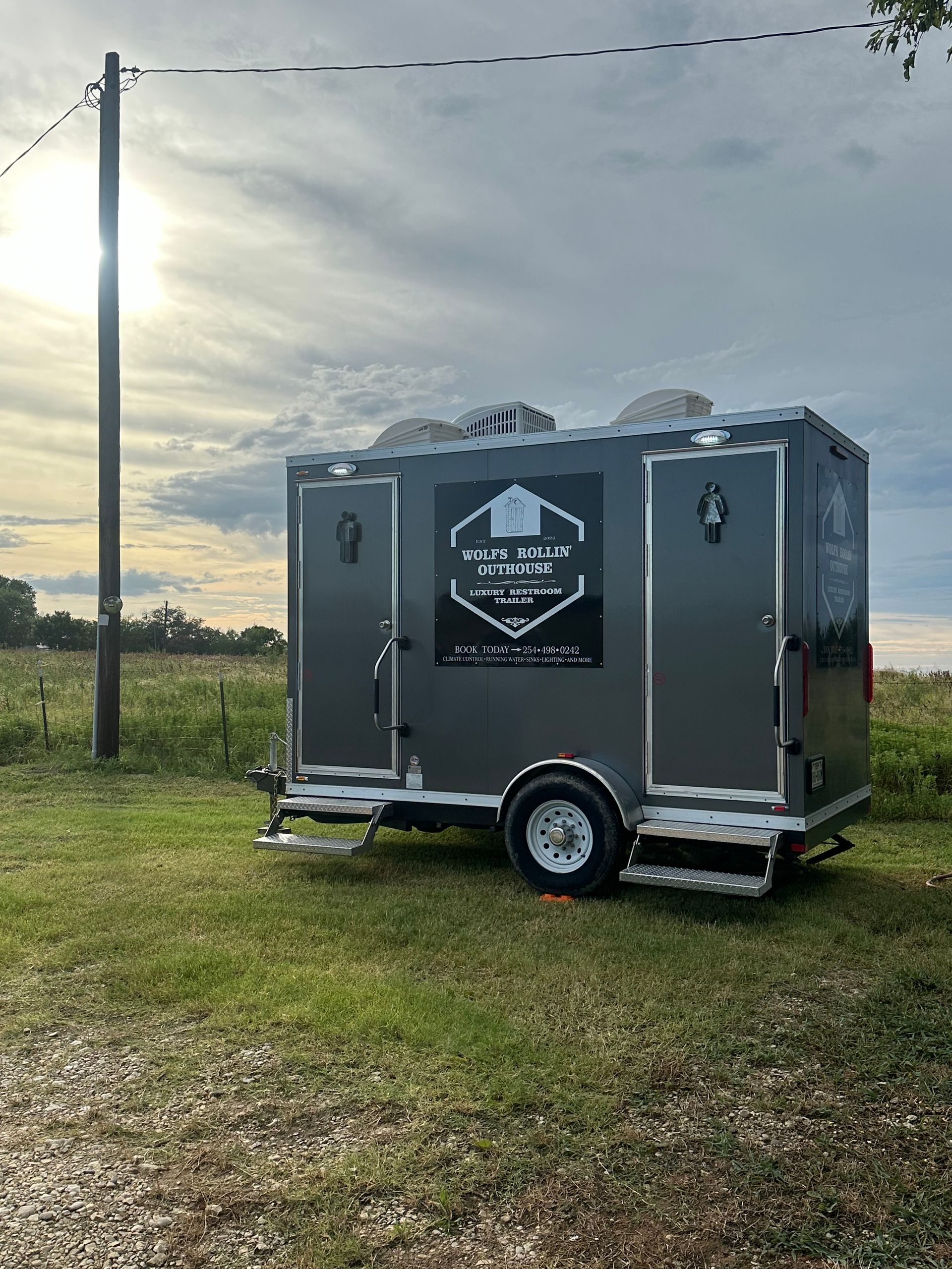 A trailer is parked in a grassy field next to a power pole.