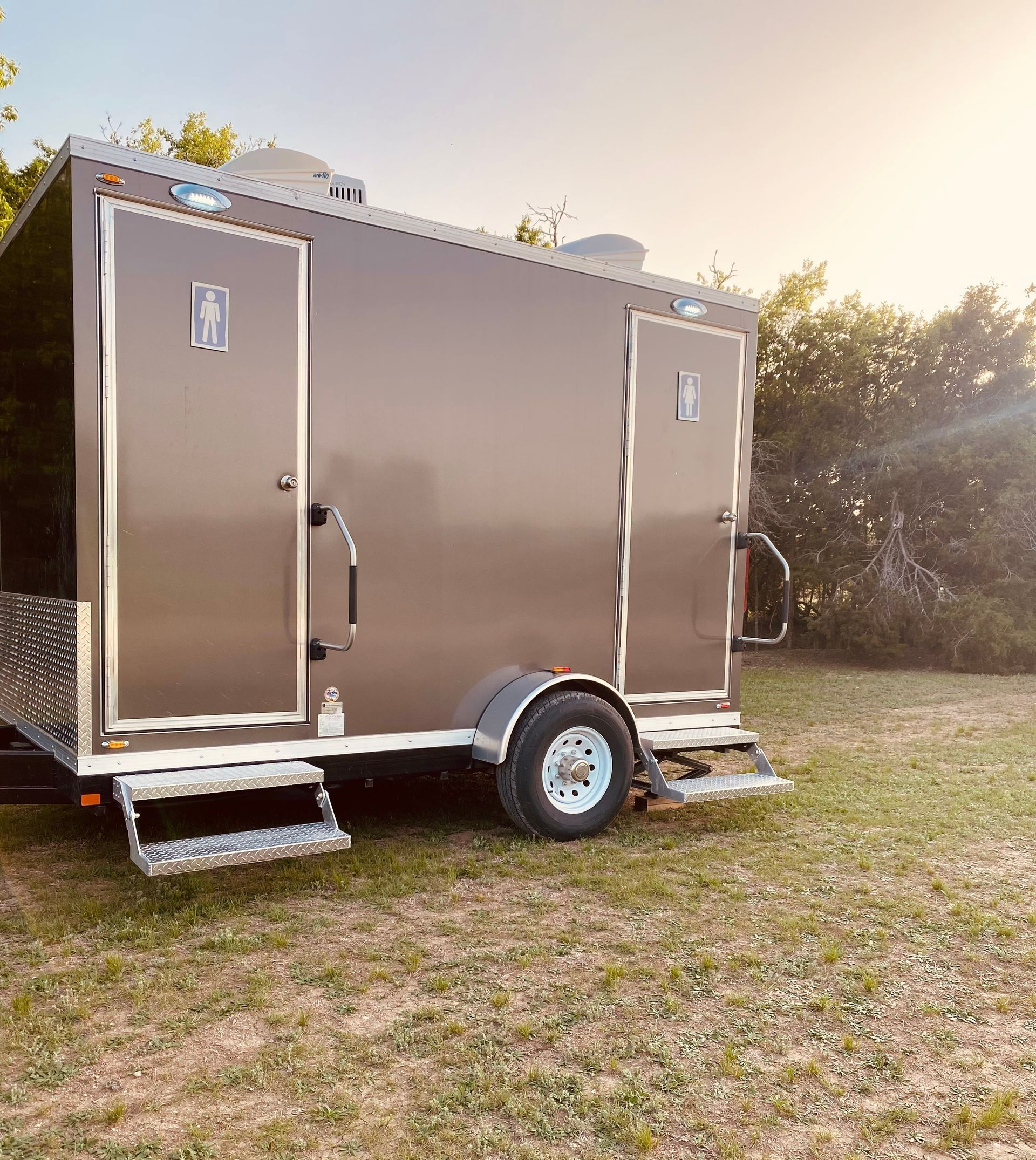 A trailer with two toilets on it is parked in a grassy field.