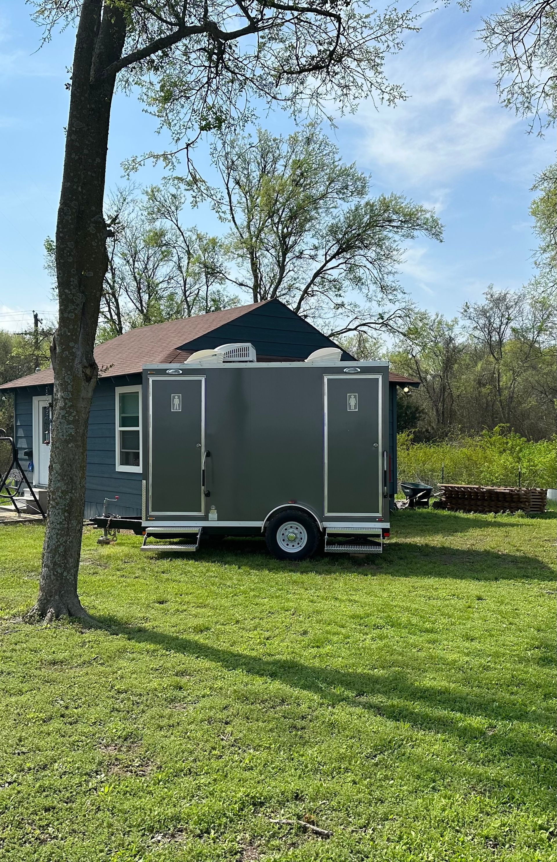 A trailer is parked in a grassy field in front of a house.