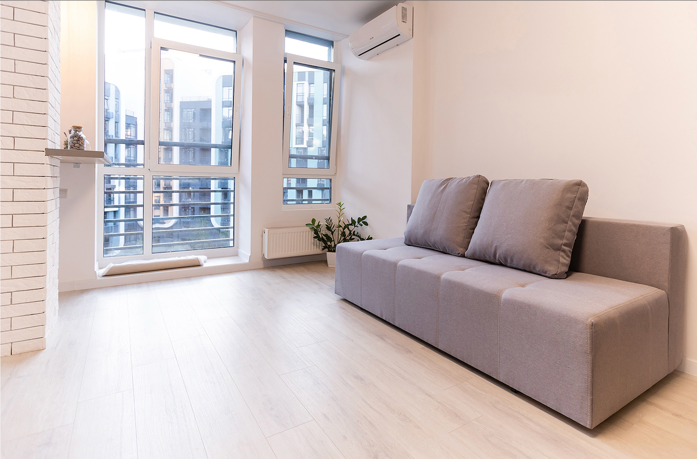 Light-filled living room with a gray sofa, large windows, and light wood flooring.