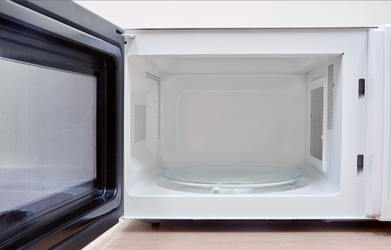 An open, empty white microwave. The door is open on the left, showing the interior with a glass plate.