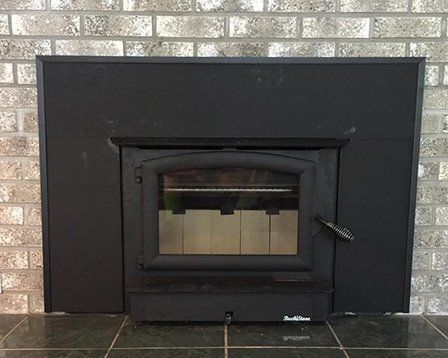 A black fireplace with a brick wall behind it