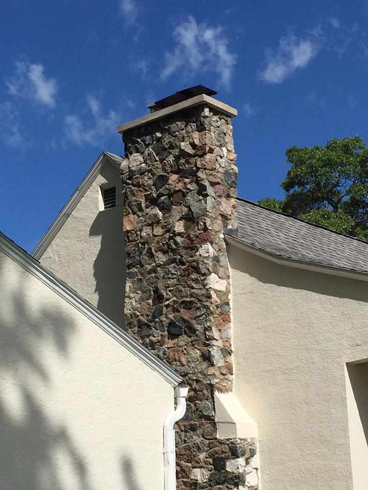 A stone chimney on the side of a house with a blue sky in the background.