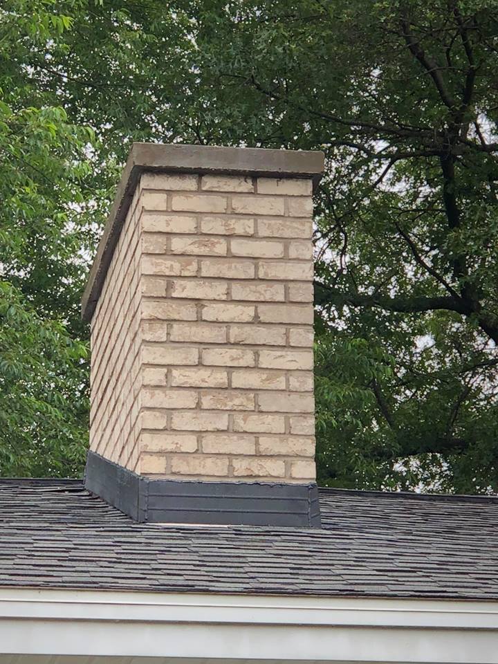A brick chimney on top of a roof with trees in the background.