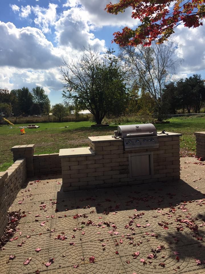 A grill is sitting on a brick patio in a park.