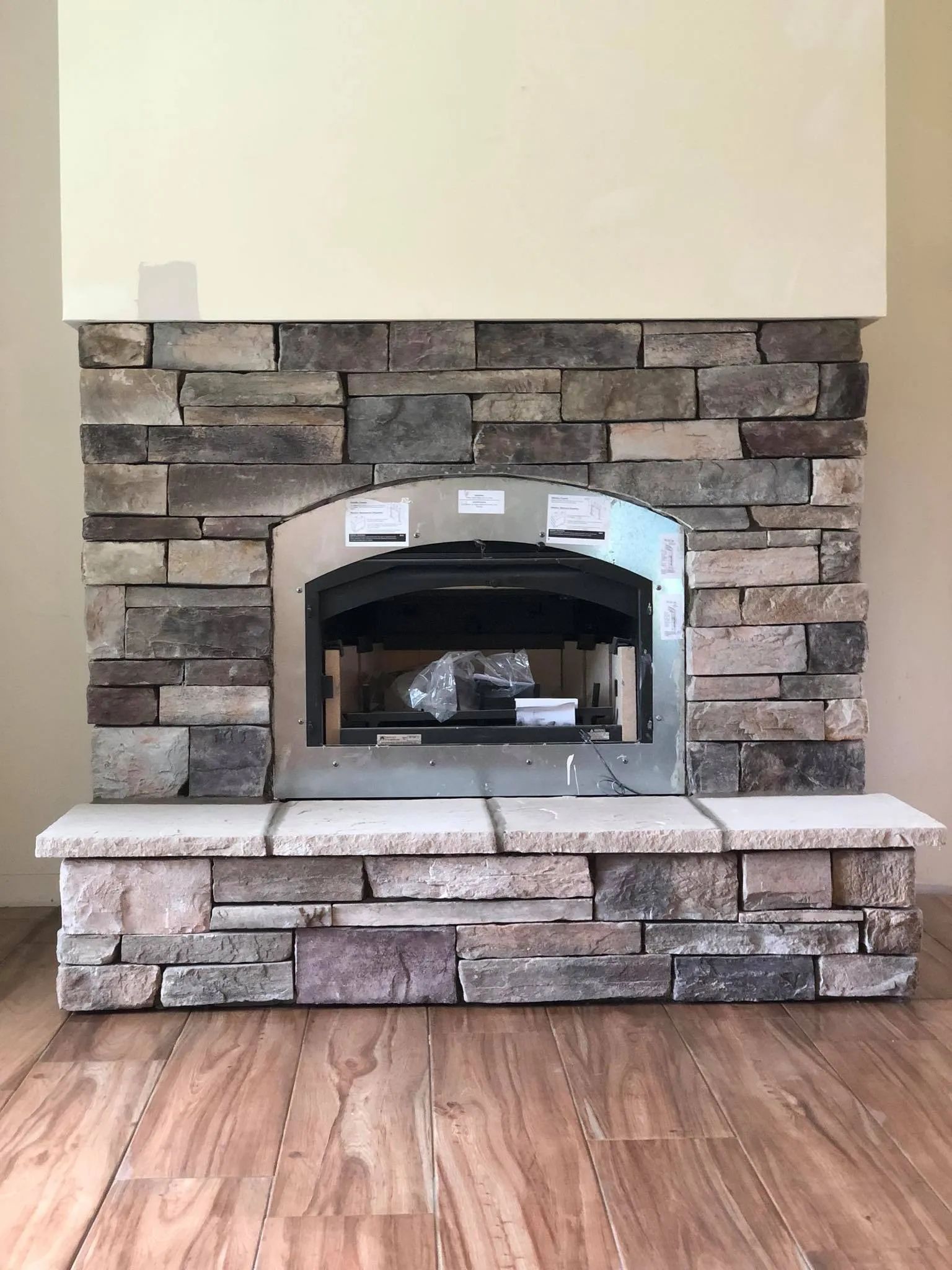 Stone fireplace with a stainless steel firebox in a room with wood flooring.