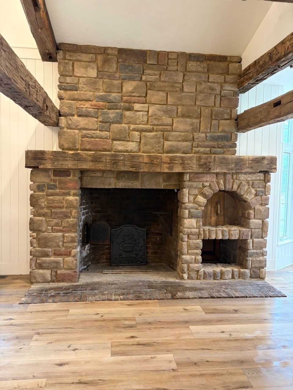Stone fireplace with large firebox and built-in wood niche in a rustic room with exposed beams and wood floor