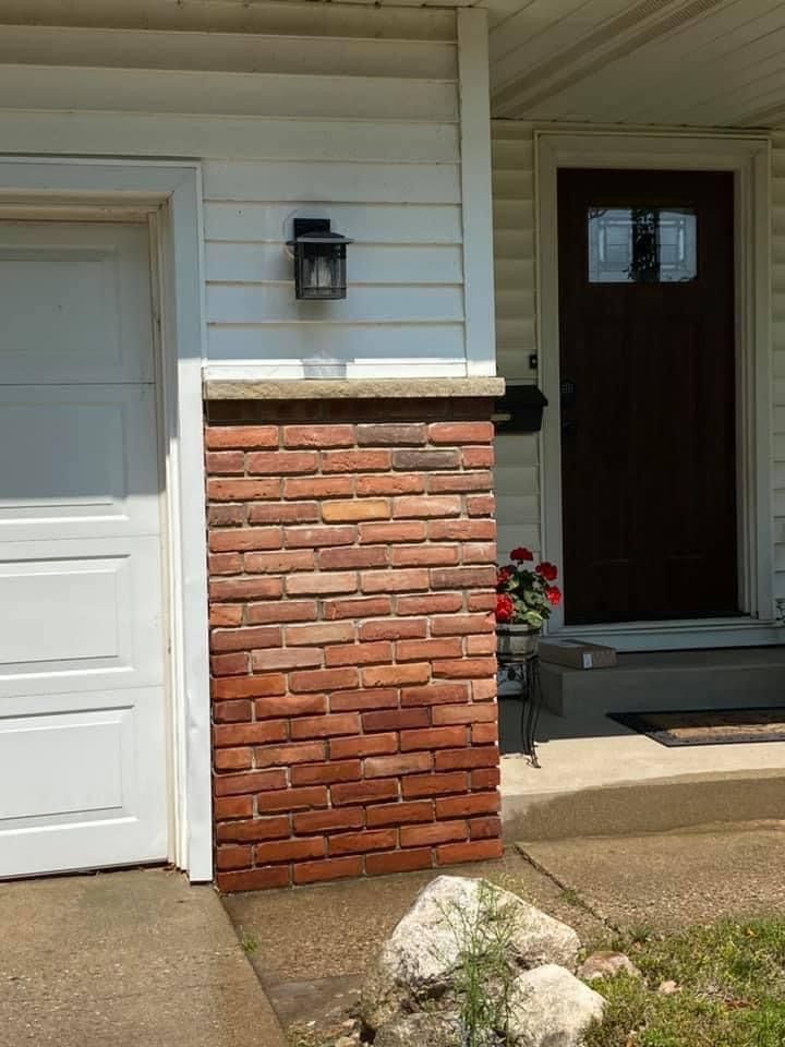 A white house with a brown door and a brick wall
