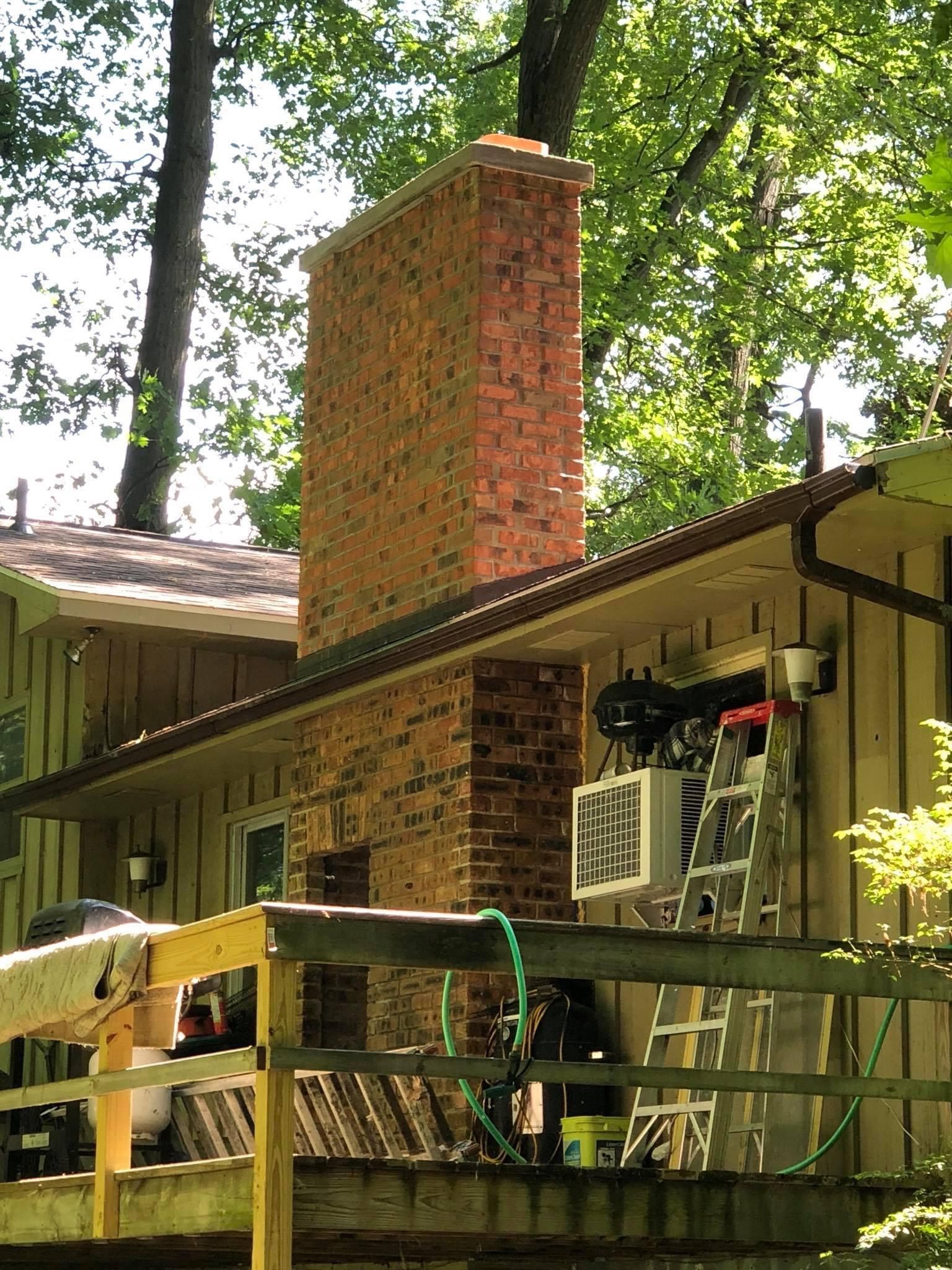 A brick chimney is on the side of a house next to a deck.