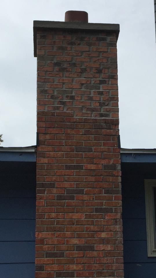 A brick chimney is sitting on the side of a blue house.