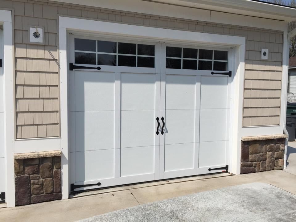 A white garage door with black handles is sitting on the side of a house.