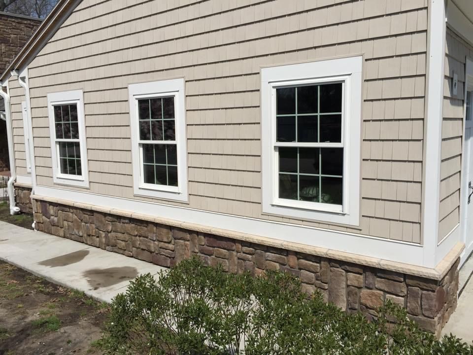 The side of a house with three windows and a stone foundation.