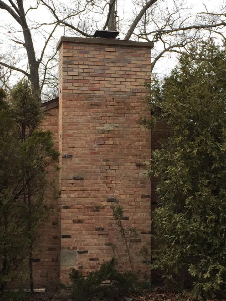 A large brick chimney on the side of a house surrounded by trees.