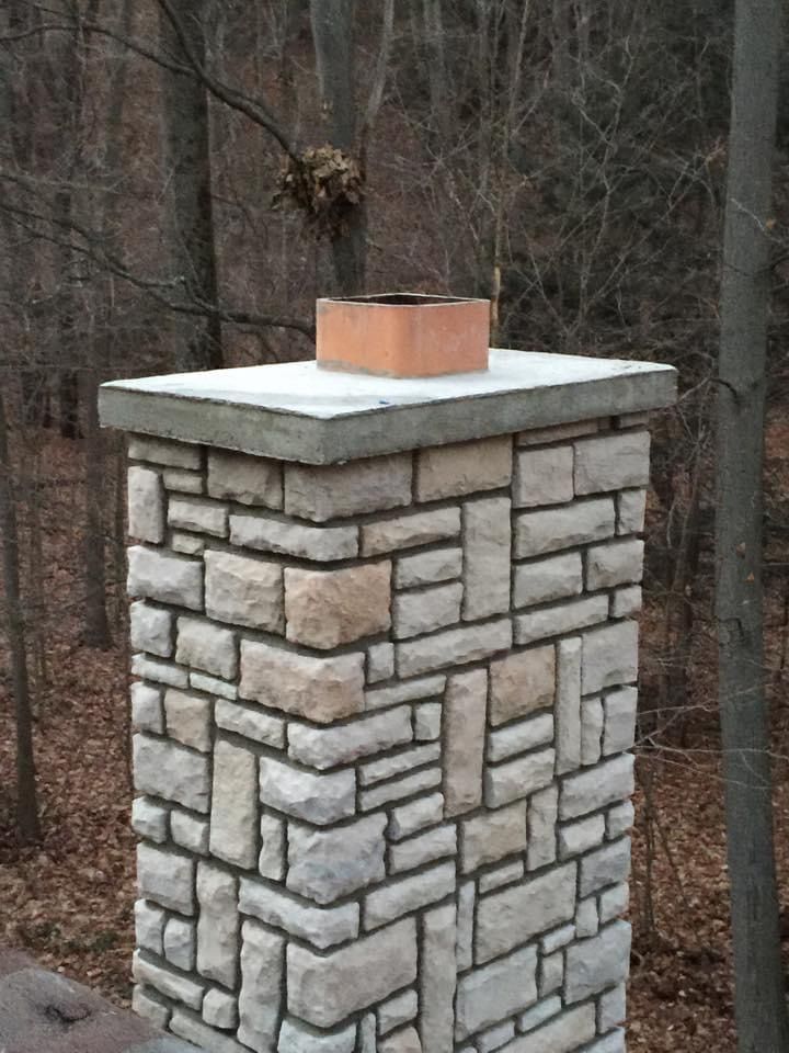 A stone chimney is sitting in the middle of a forest.