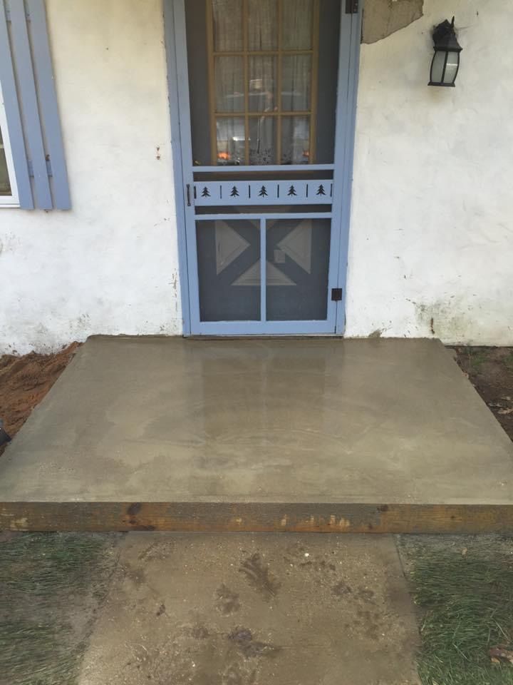 A concrete walkway leading to a screen door of a house