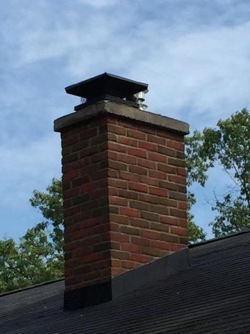 A brick chimney on top of a roof with trees in the background