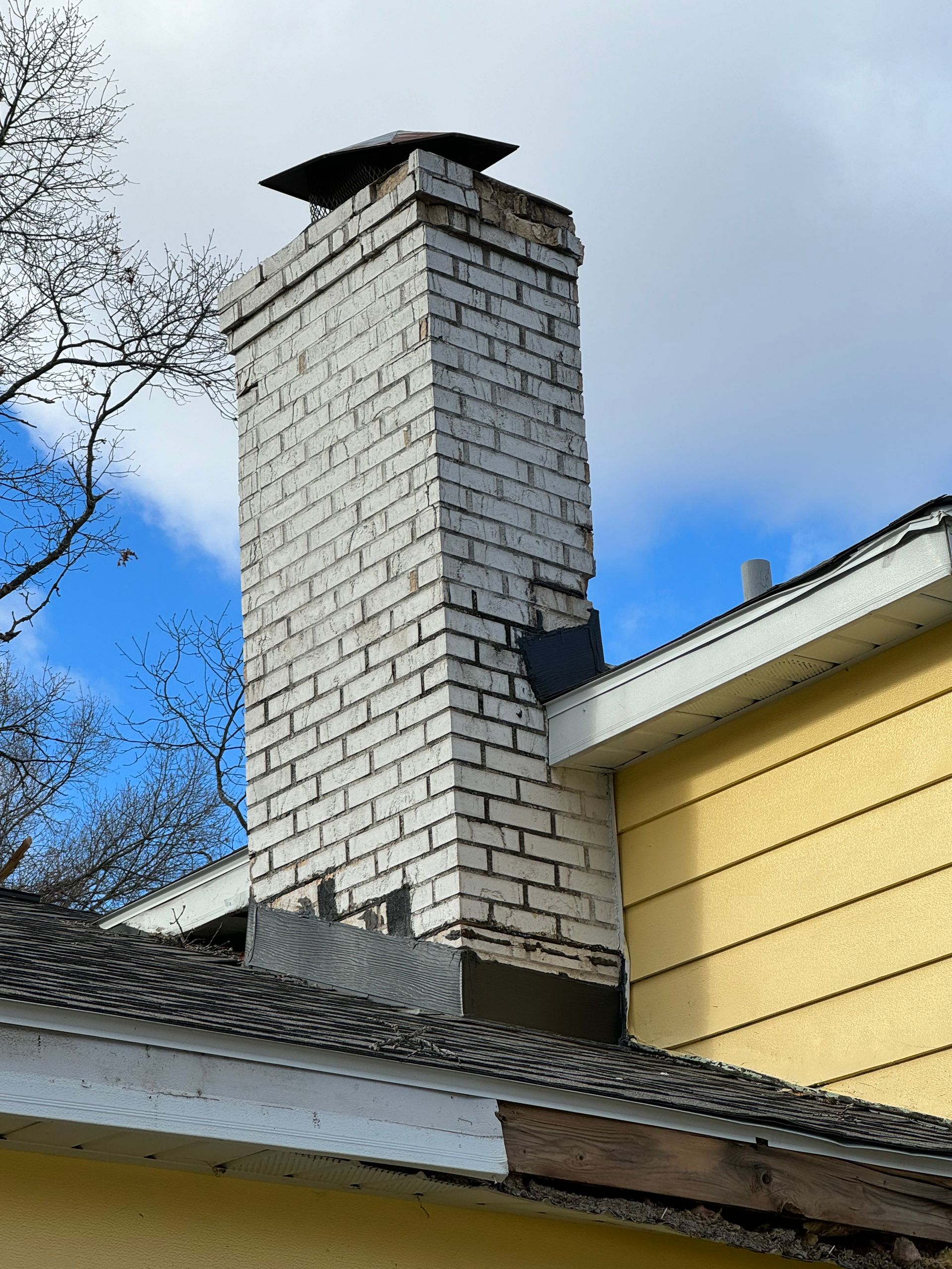 A white brick chimney is on the side of a yellow house.