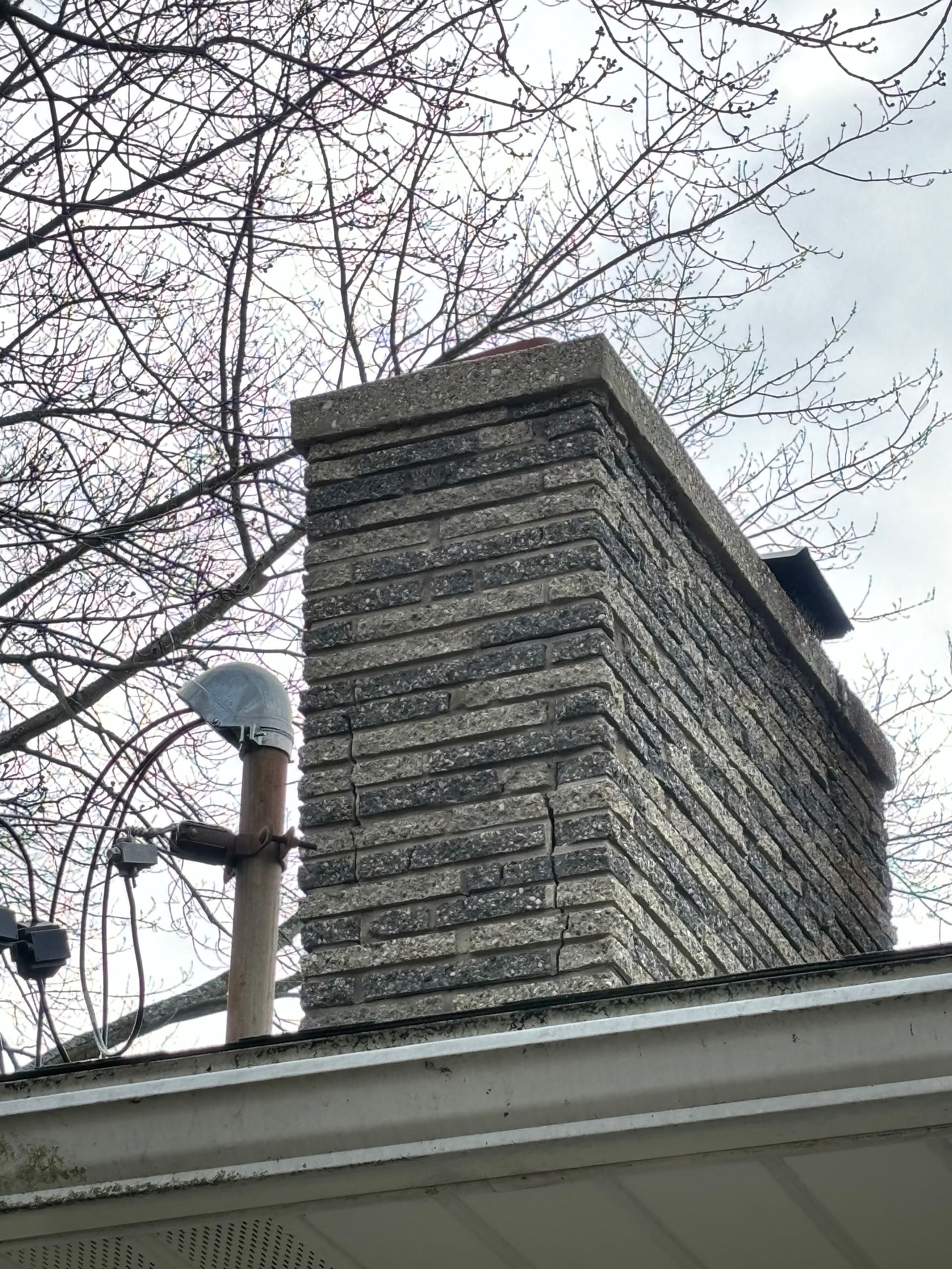 A chimney on the roof of a house with trees in the background.