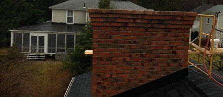 A brick chimney is sitting on top of a roof next to a house.