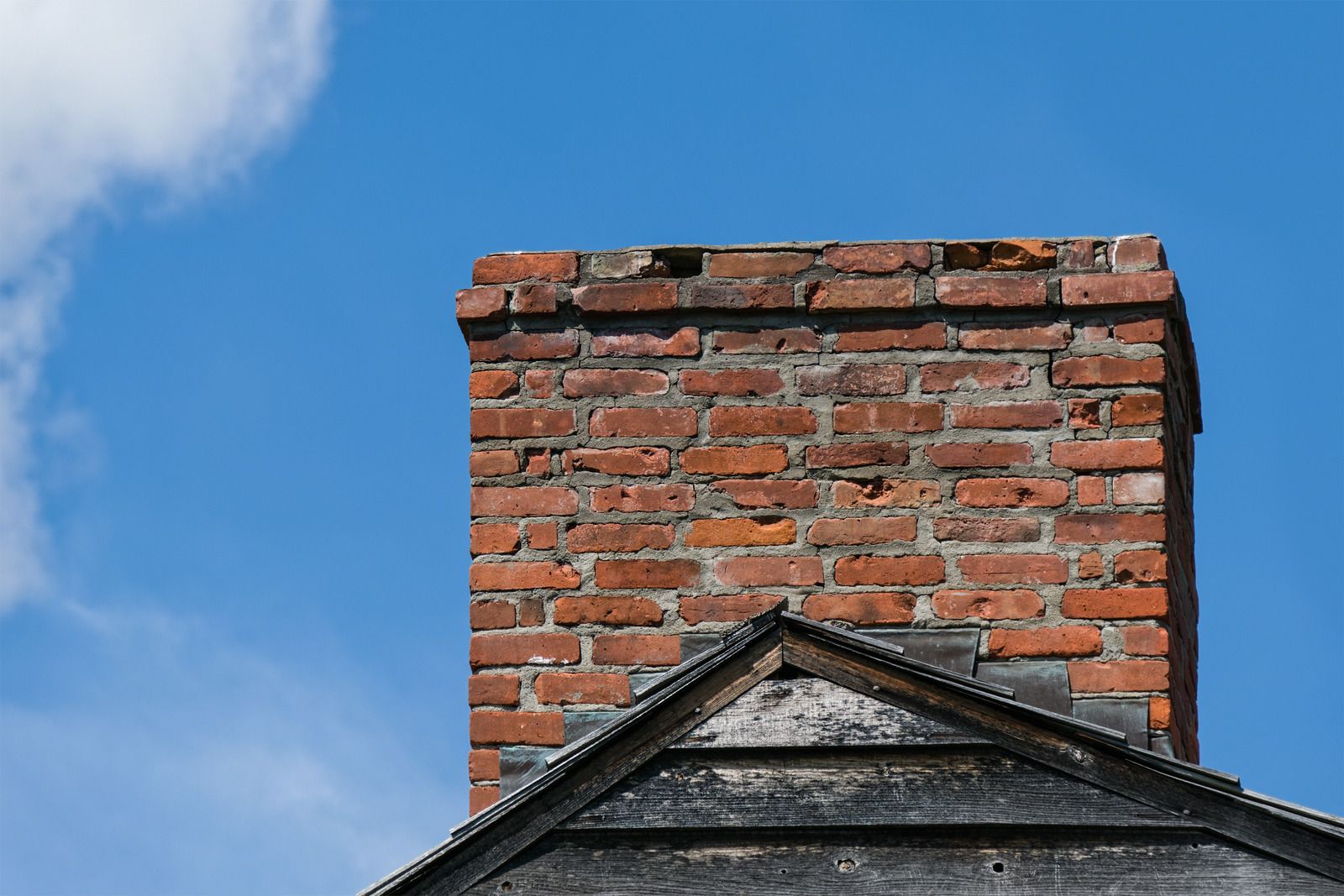 Brick chimney on a roof against a blue sky.