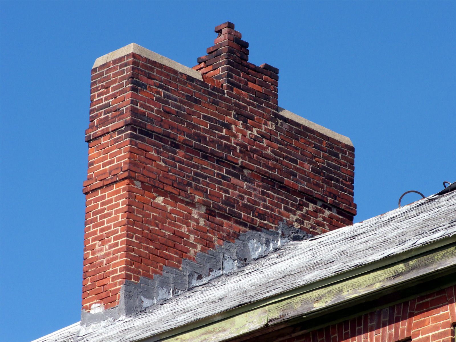 Brick chimney with a decorative top on a roof against a blue sky.