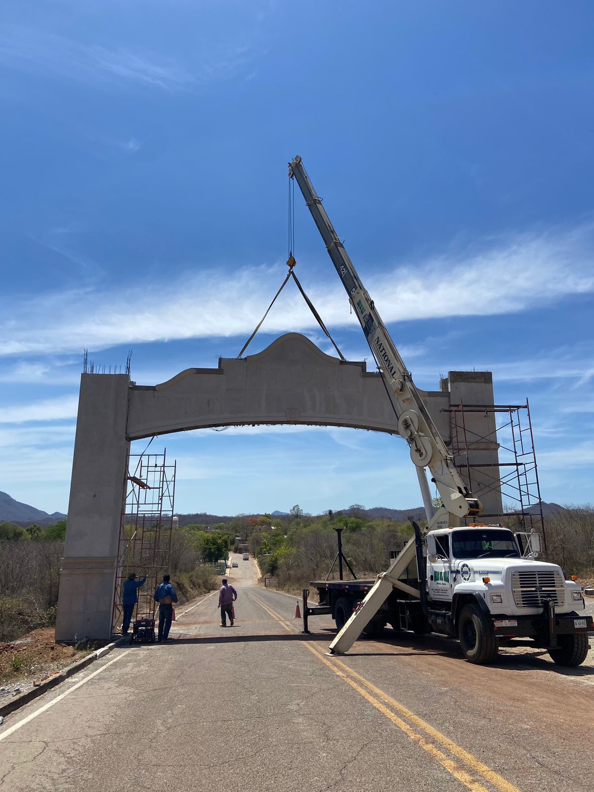 Una grúa está levantando un arco de hormigón sobre una carretera.