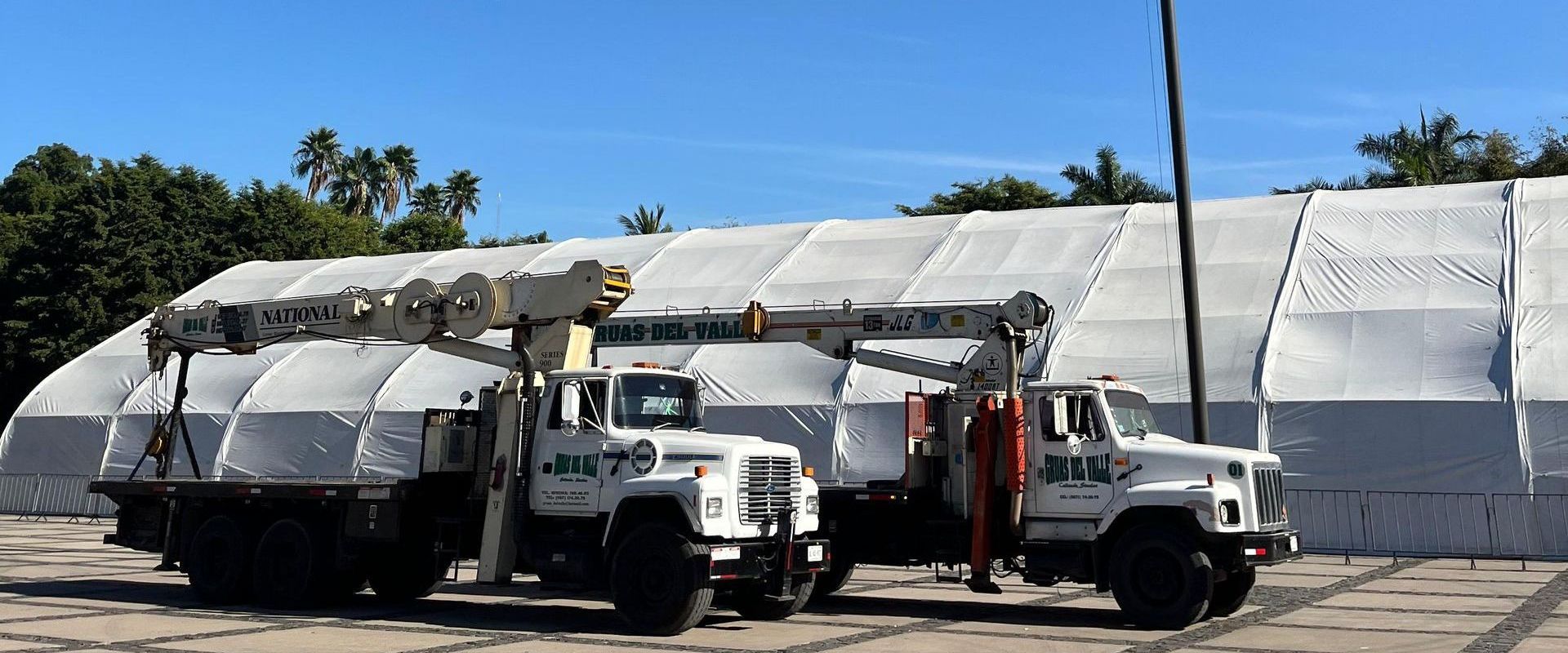 Dos camiones están estacionados frente a una gran carpa blanca.