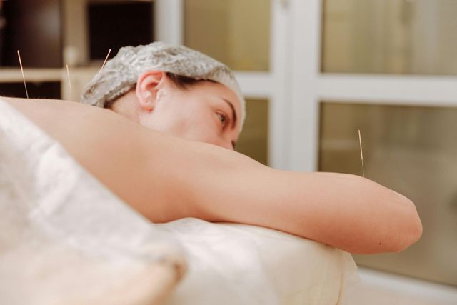 Person relaxing in a bathtub with a shower cap, leaning on the tub edge by a window
