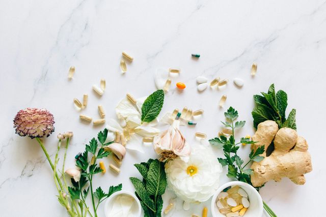 Herbs, ginger, flowers, and sliced garlic arranged on a white marble surface