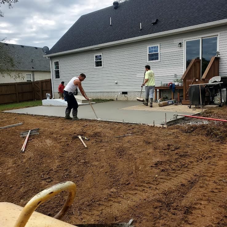 Construction workers pouring concrete for a patio in a backyard setting.