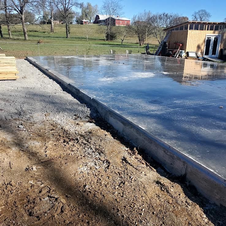 Newly poured concrete slab with wooden formwork, near a building under construction.