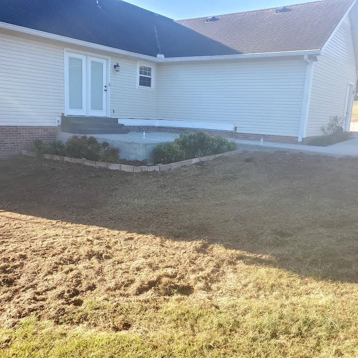 Exterior of a beige house with a concrete patio, landscaping, and brown lawn on a sunny day.