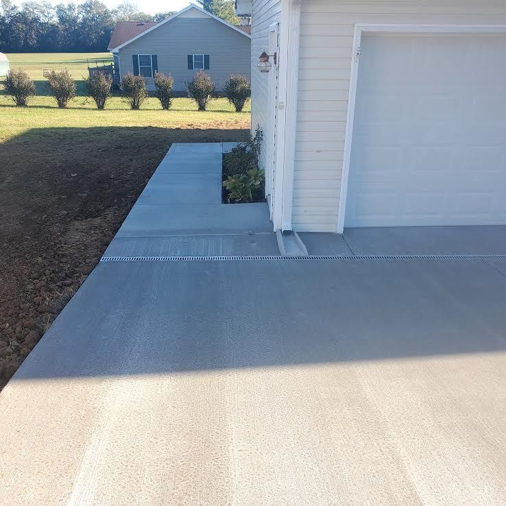 Concrete driveway and sidewalk next to a white garage. A house with a blue roof is in the background.