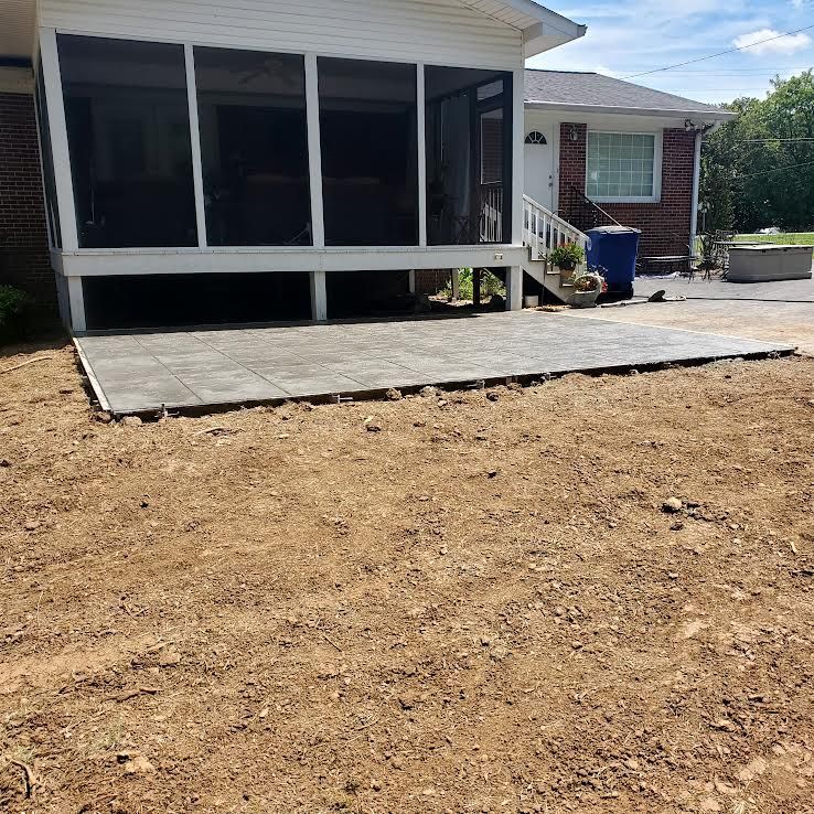 A paved patio with a dirt yard next to a screened porch attached to a brick house.