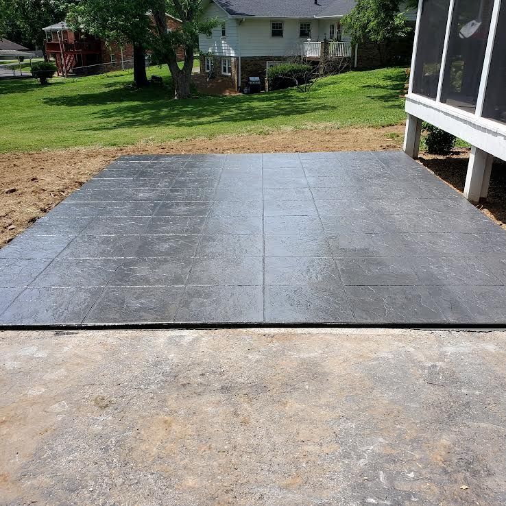 Gray concrete patio next to a porch with a green lawn and house in the background.