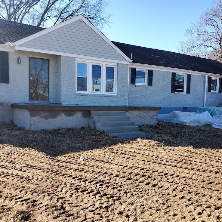 A light blue brick ranch home with steps, a porch, and new siding. The front yard is dirt.