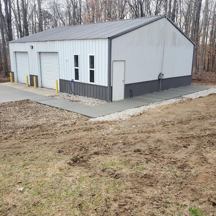 White industrial building with gray trim and doors on a concrete pad with a gravel border.