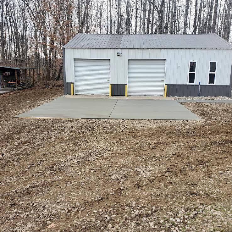 Two-bay garage with concrete pad, surrounded by dirt and trees.