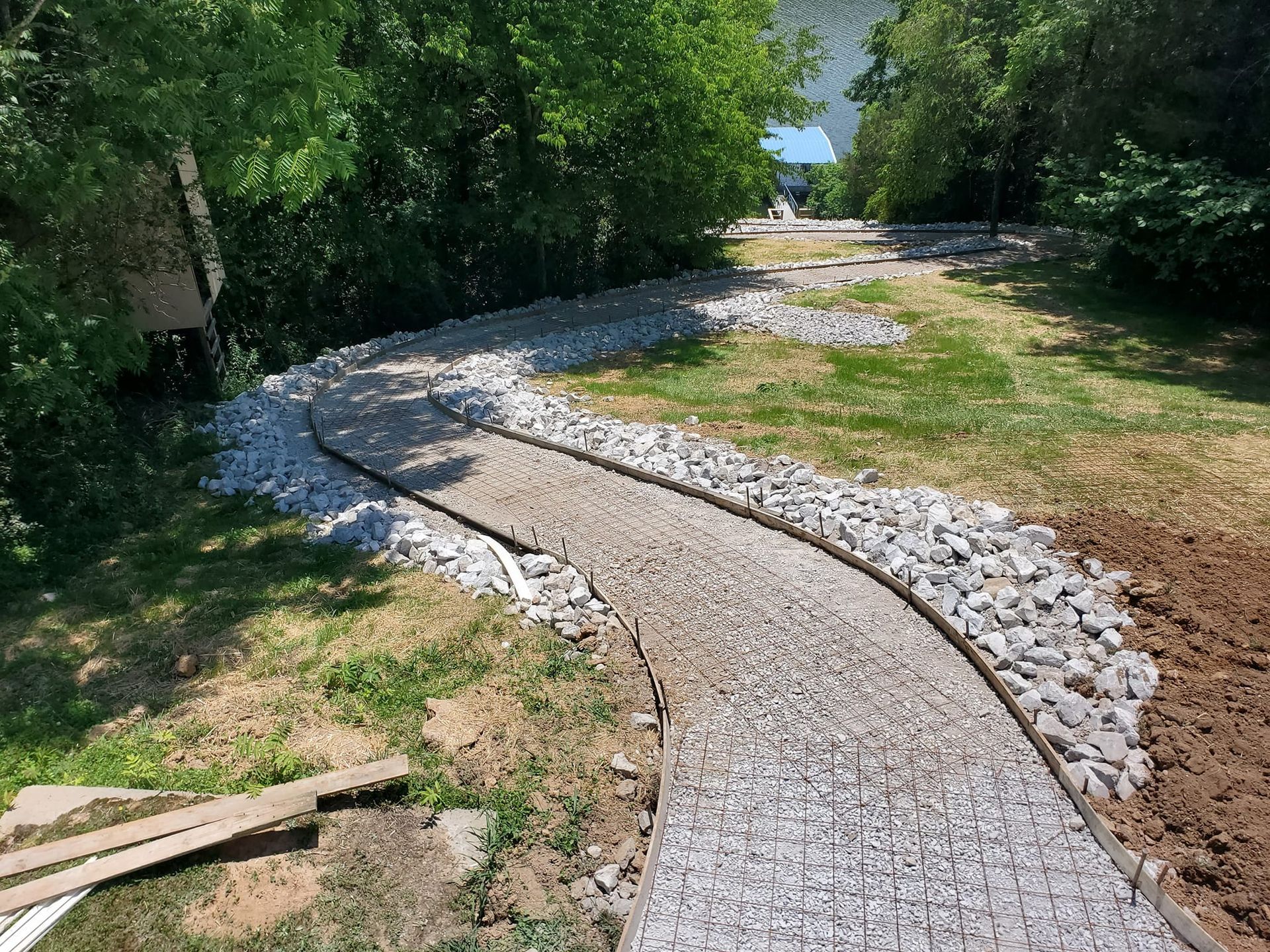 A gravel pathway curves through a grassy area, bordered by rocks and trees.