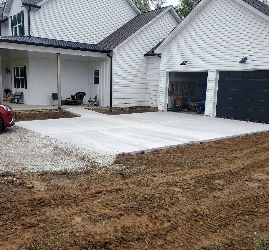New concrete driveway at white house with garage, gravel border, and dirt yard.