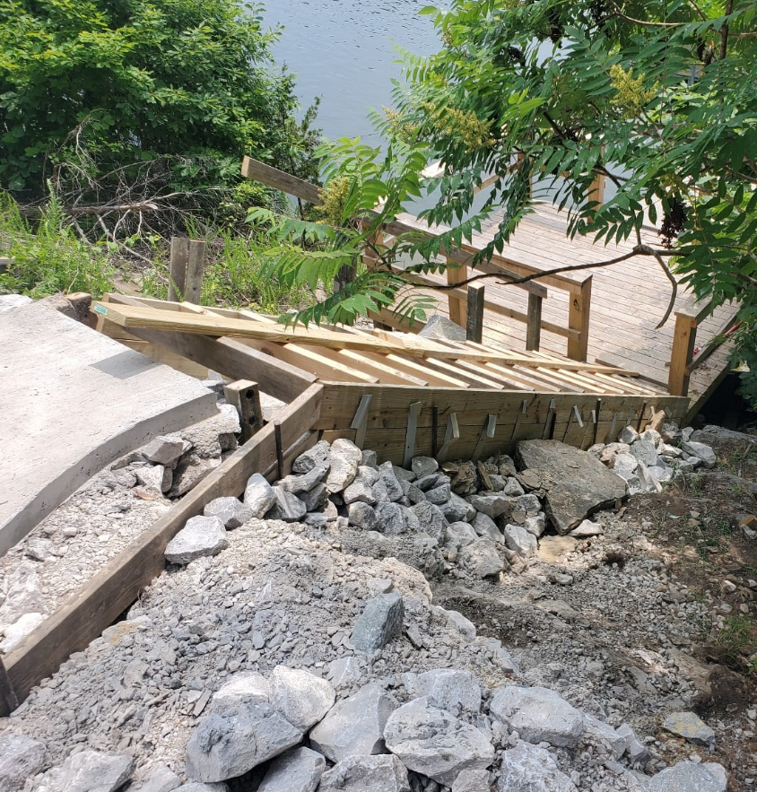 Staircase under construction leading down to water, with rocks and debris.