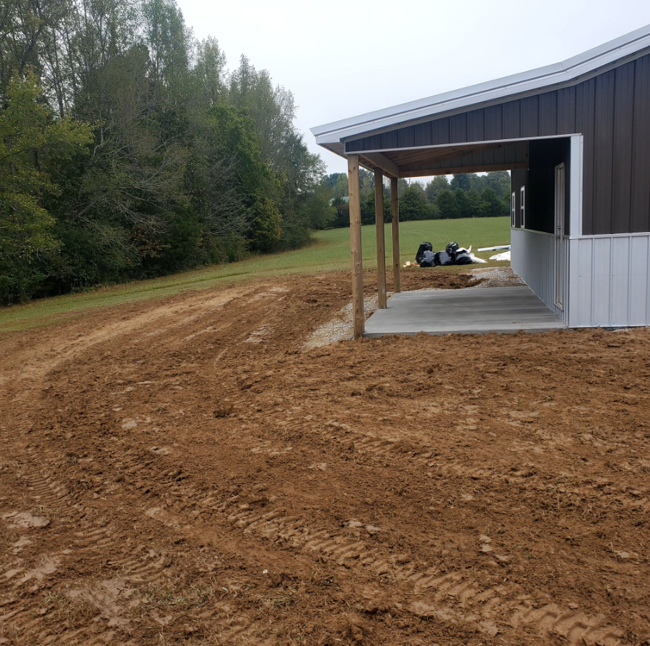 A brown and white building with a covered porch on a dirt lot. Trees in the background.