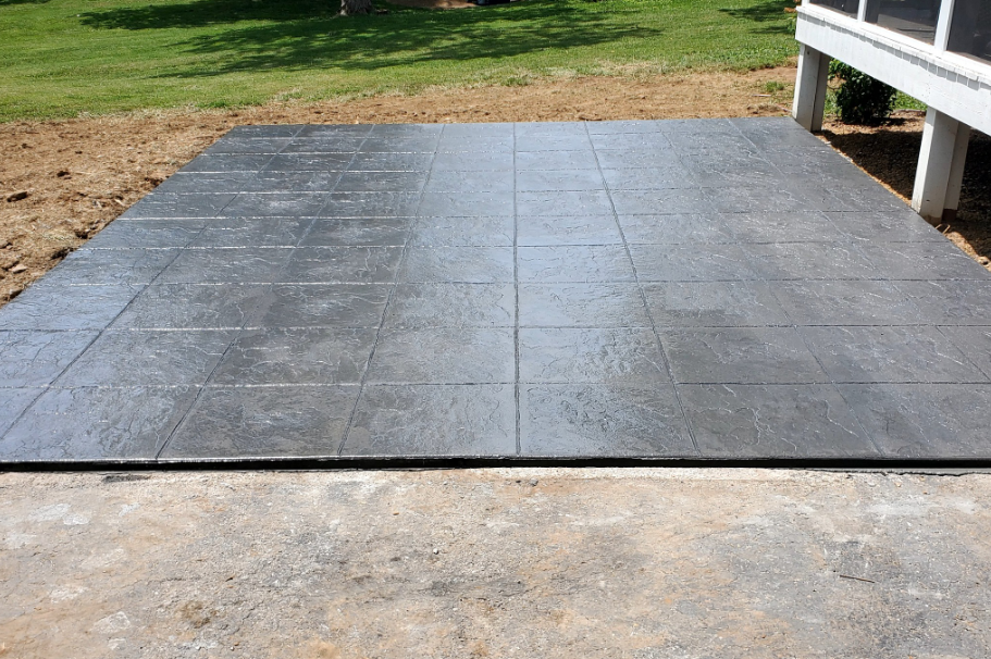 Newly installed, dark gray stamped concrete patio next to a concrete foundation.