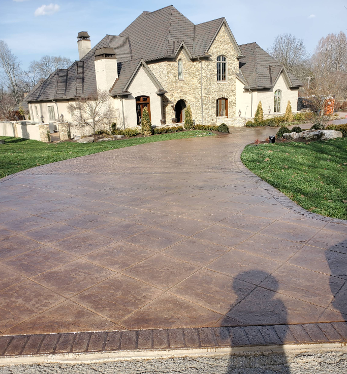 Large stone house with long patterned driveway, sunny day.
