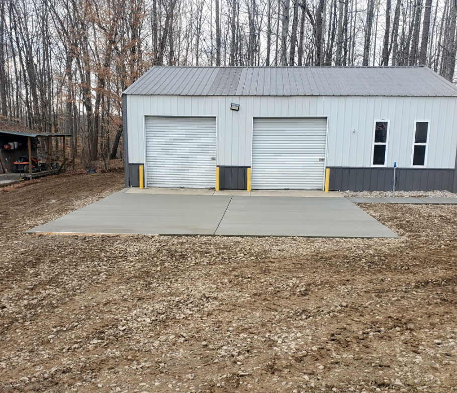 A two-car garage with white doors, a concrete pad, and gravel ground.