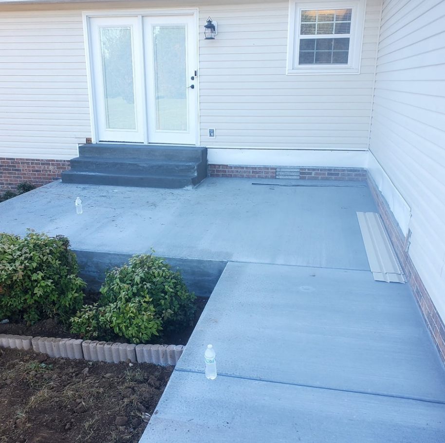 Newly poured concrete patio and walkway leading to a house with white doors, window, and exterior.