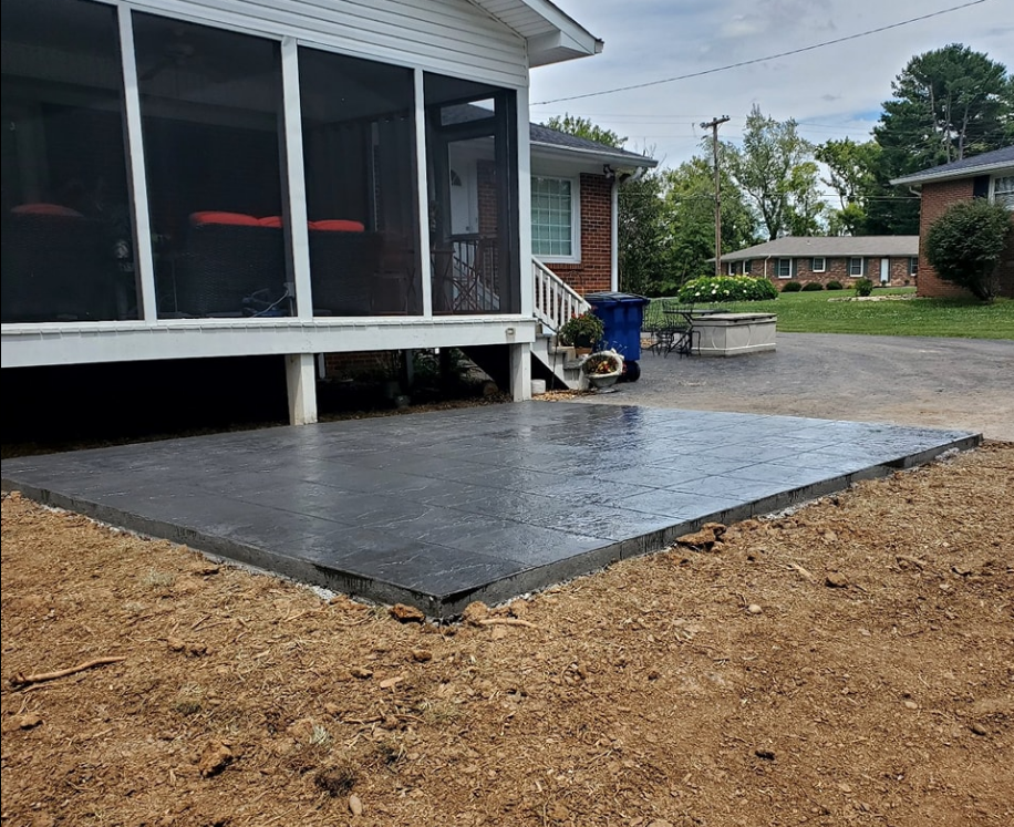 Newly poured concrete patio next to a house with a screened porch; wet surface, dirt surrounds.