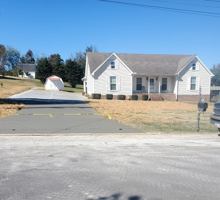 A white house with a newly poured concrete driveway on a sunny day.