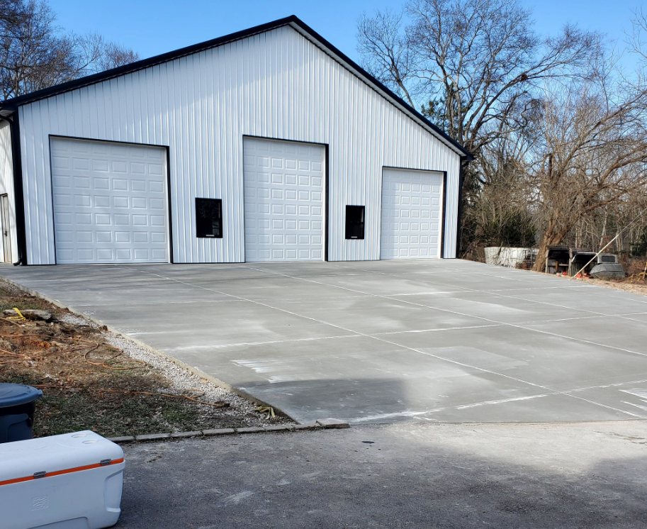 White metal building with three garage doors and concrete driveway.