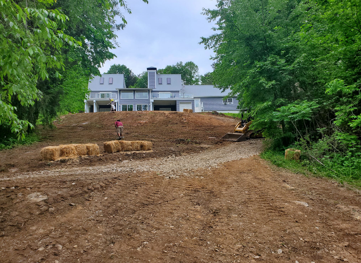 Dirt road and hillside construction site; large house in background.